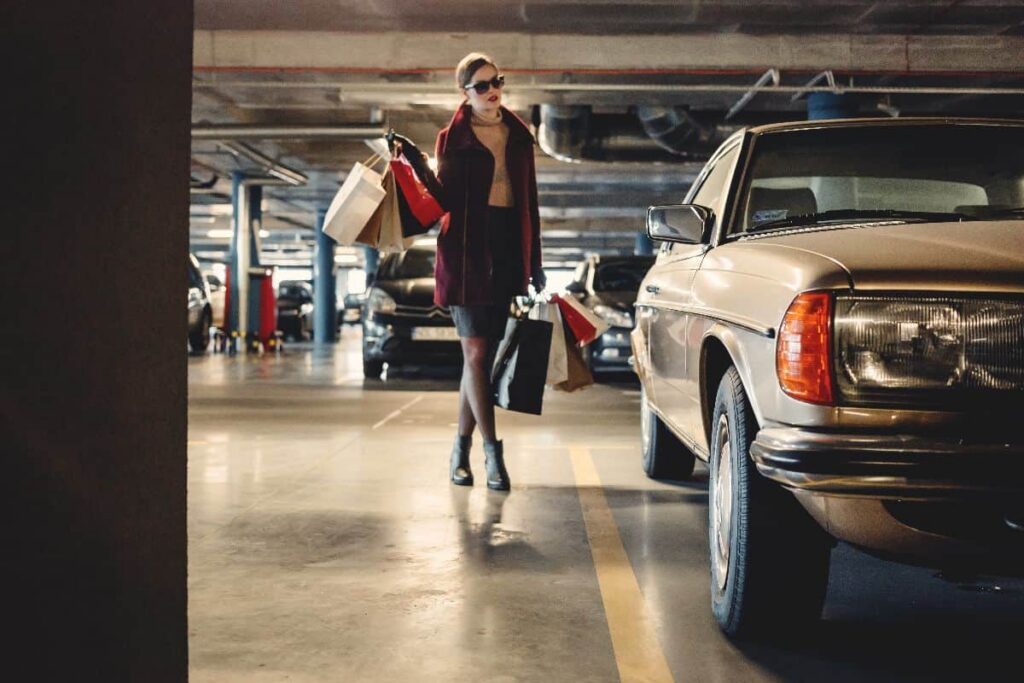A lady standing with shopping bags next to a car